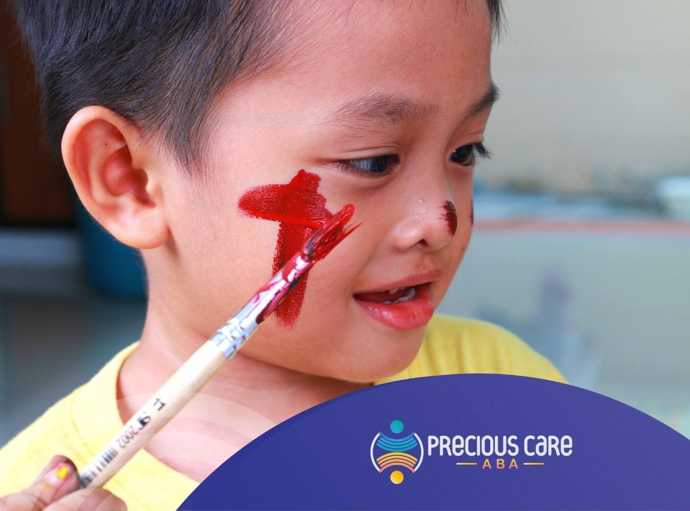 A child with red paint on his face smiles in ABA therapy.