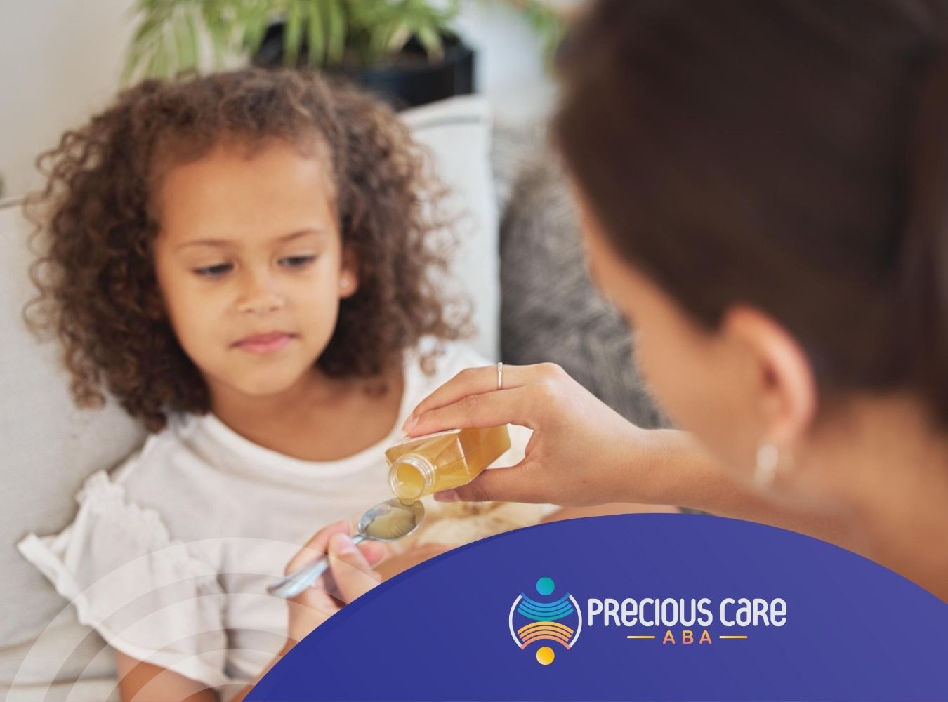 A caregiver administers a dose of liquid medicine to a child sitting on a couch.