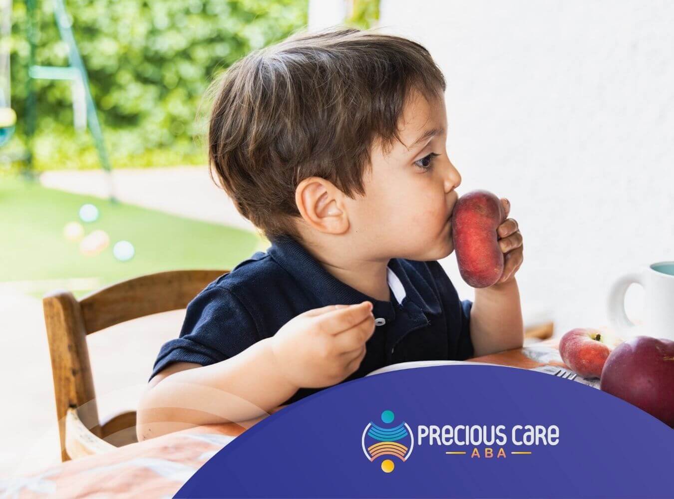 A young boy with autism is sitting at a table eating an apple and fruit salad in ABA therapy.
