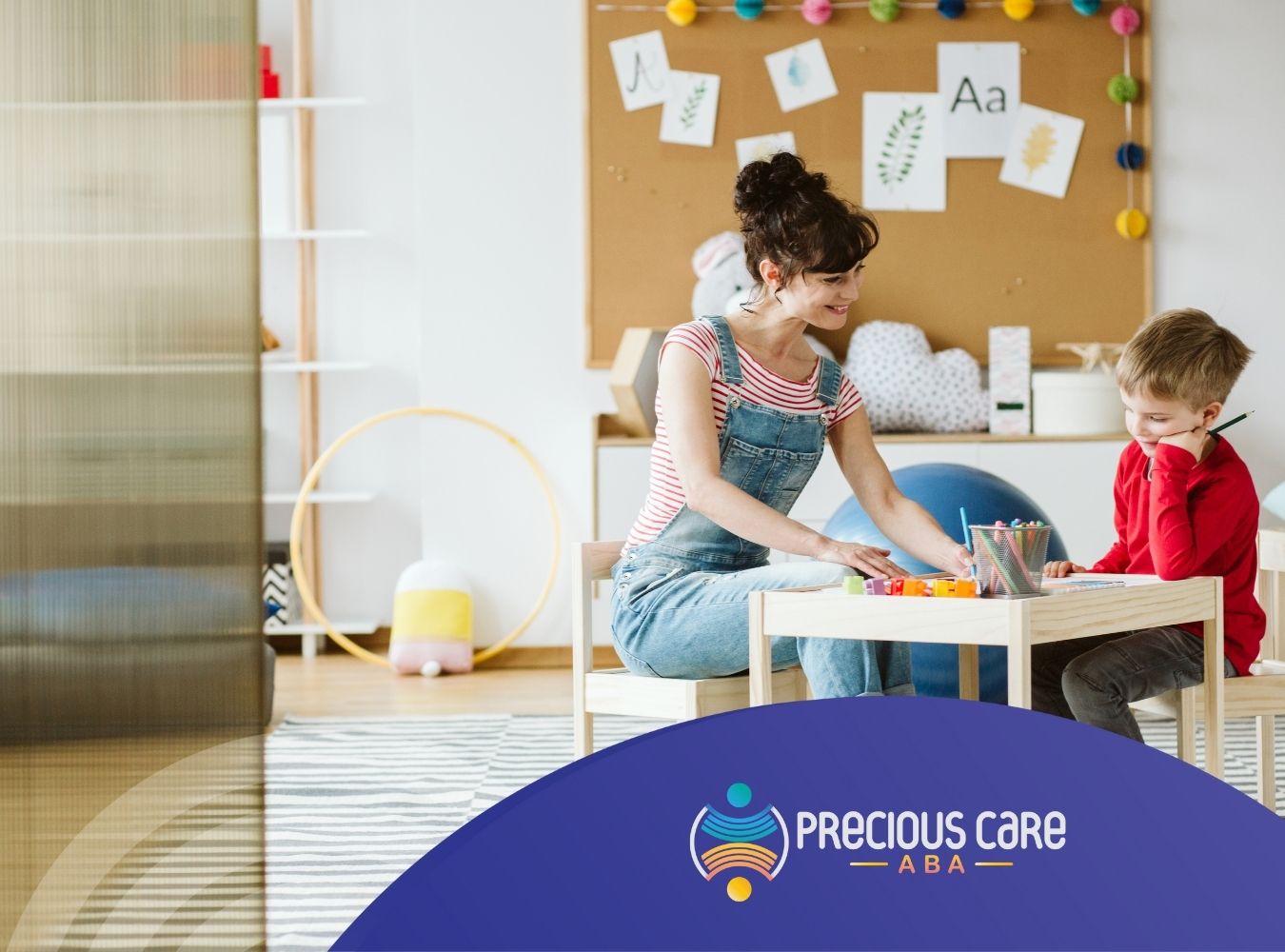 An ABA therapist guiding a little boy drawing, sitting on a table.