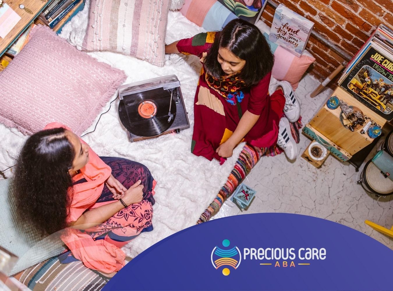 Two autistic girls sitting on a bed listening to a vinyl record while talking in a decorated room.
