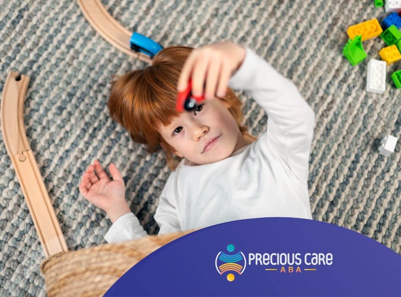 Autistic child lying on rug playing with toy car during ABA therapy.