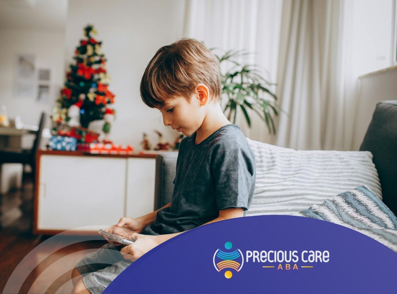 Young autistic boy sitting on a couch using a smartphone near a Christmas tree in Colorado.