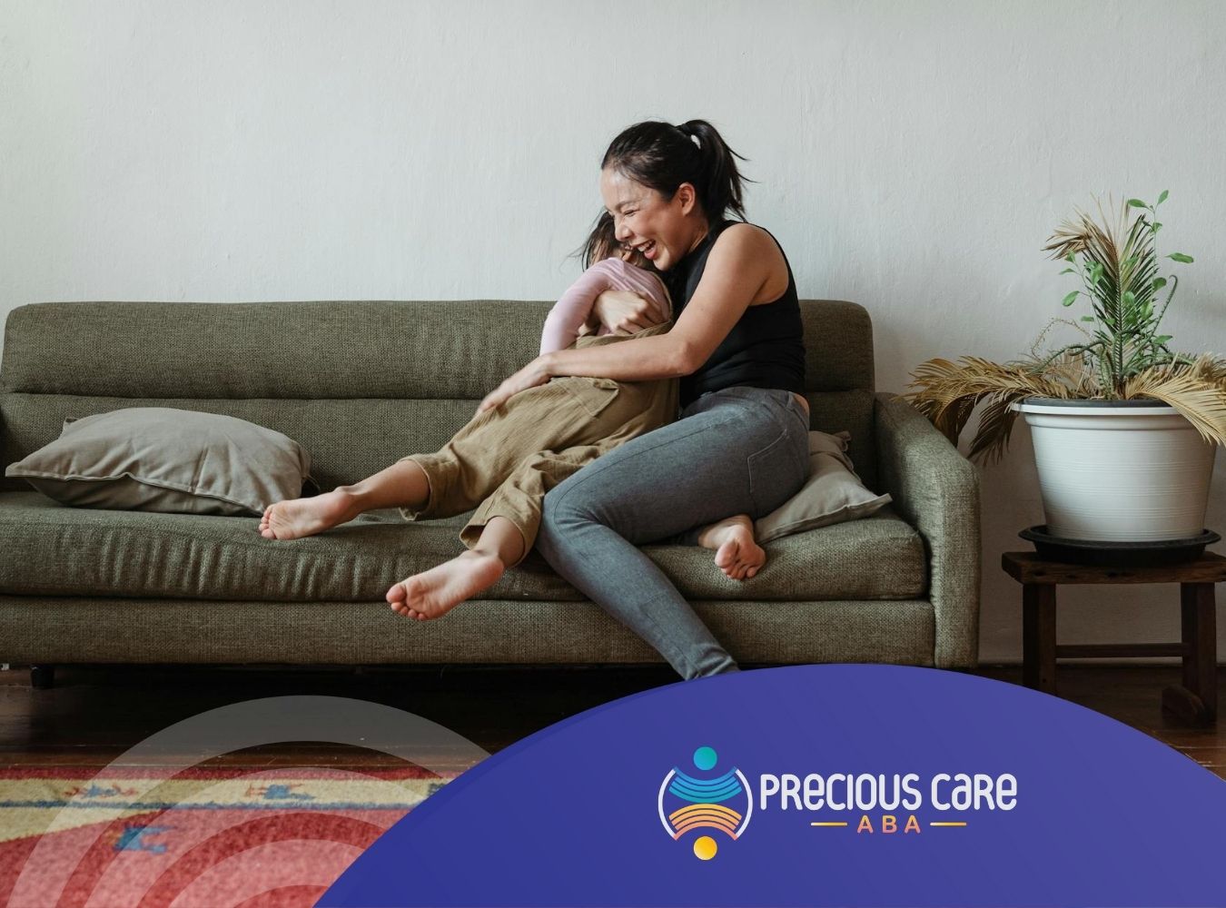 A mother laughing while playfully holding her autistic child on a couch during in-home ABA therapy in NJ.