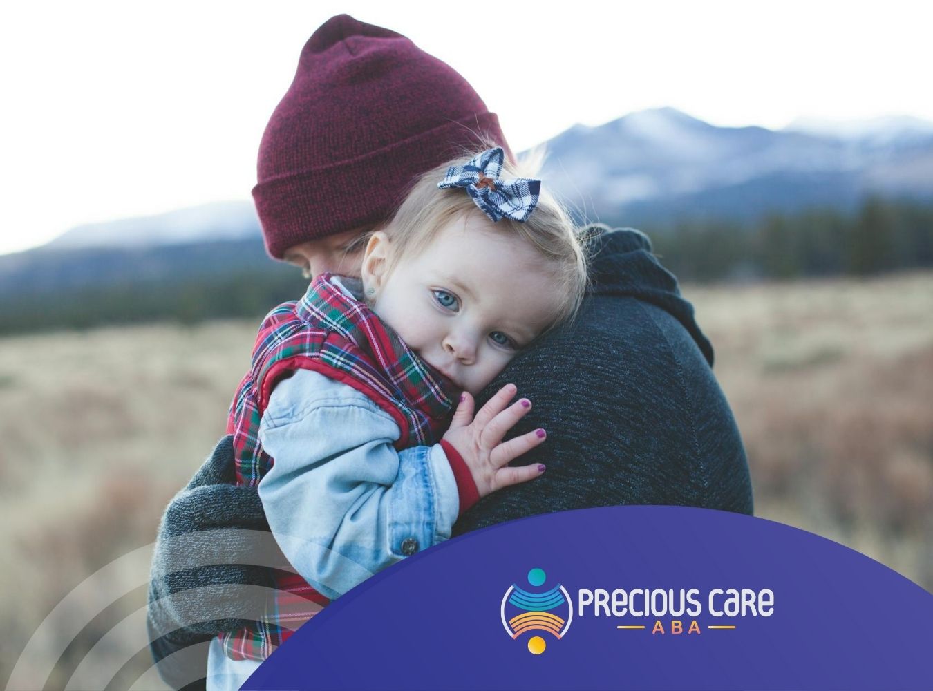 An autistic baby resting on their parent’s shoulder, looking straight at the camera outdoors in New Jersey.