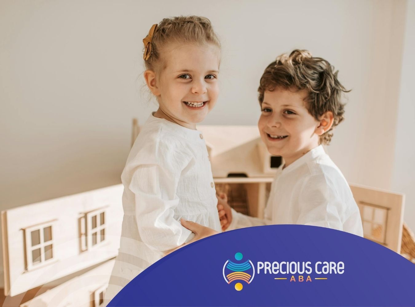 Two autistic kids smiling while holding hands in front of a wooden dollhouse during in-home ABA therapy.