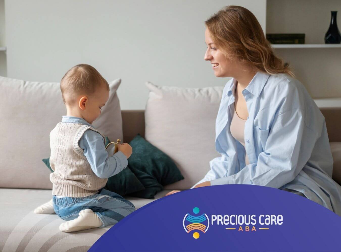 ABA therapist smiling at toddler playing with a toy on the couch in ABA therapy.