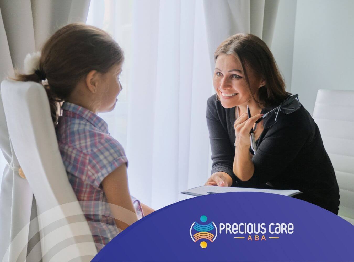 Smiling ABA therapist talking with a young girl holding a clipboard in ABA therapy.