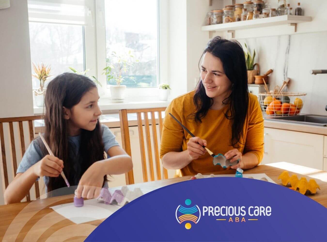 A BCBA and a girl sit at a kitchen table, painting egg cartons with bright colors in ABA therapy.