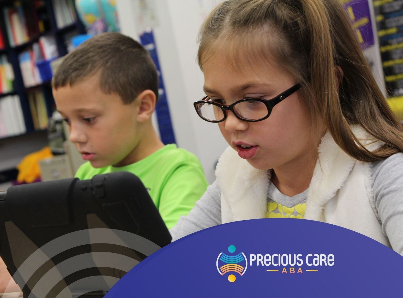 Two focused children, a girl in glasses and a boy in a green shirt, use tablets in a classroom setting. Shelves of colorful books are visible in the background.