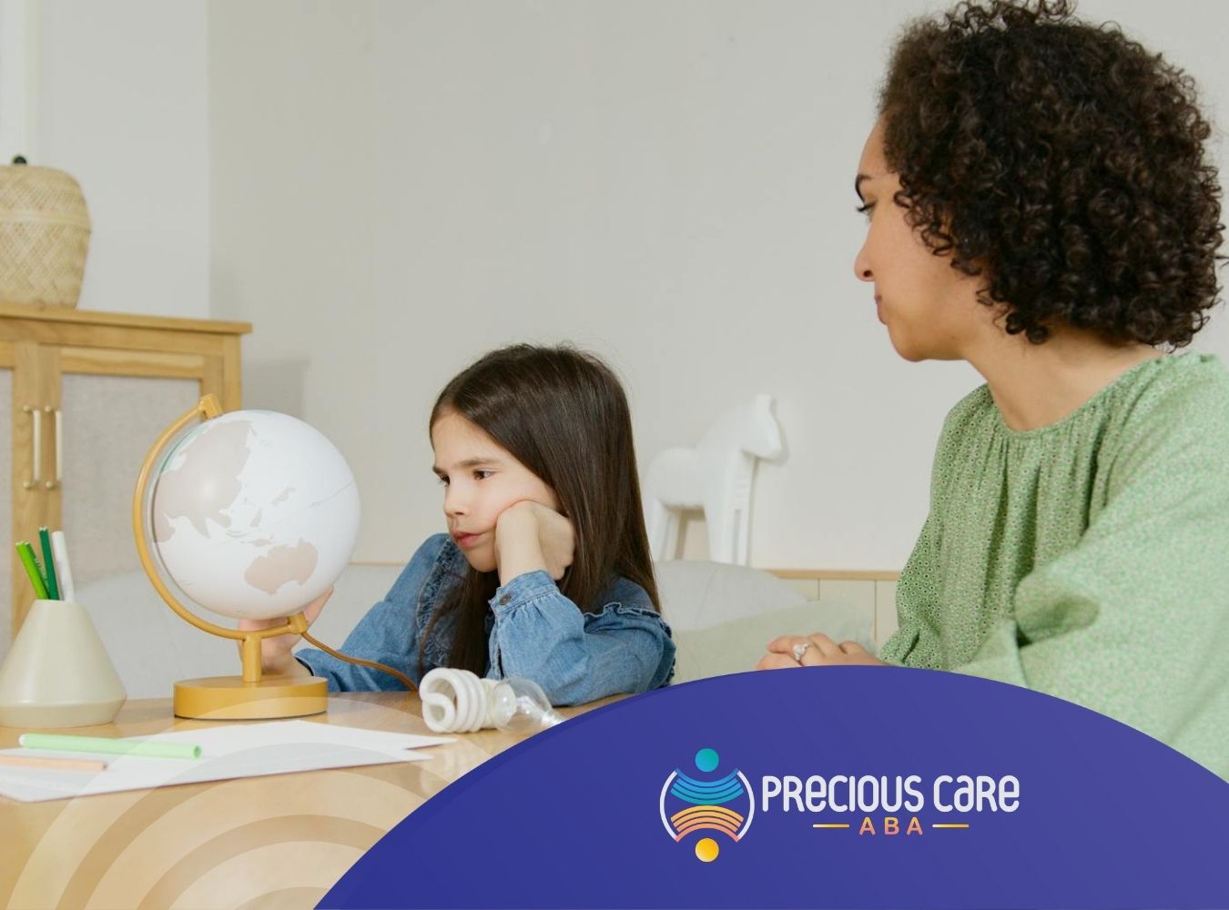 An autistic child looking at globe with a parent beside her during learning activity in ABA therapy session in MD.