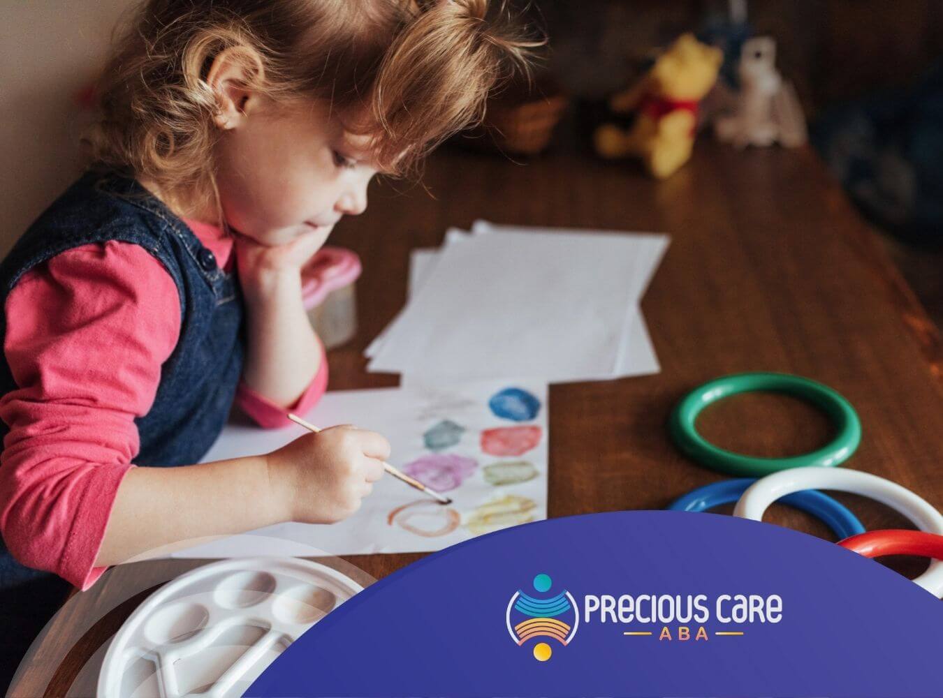 A little girl with autism painting on paper with watercolor paints in ABA therapy.