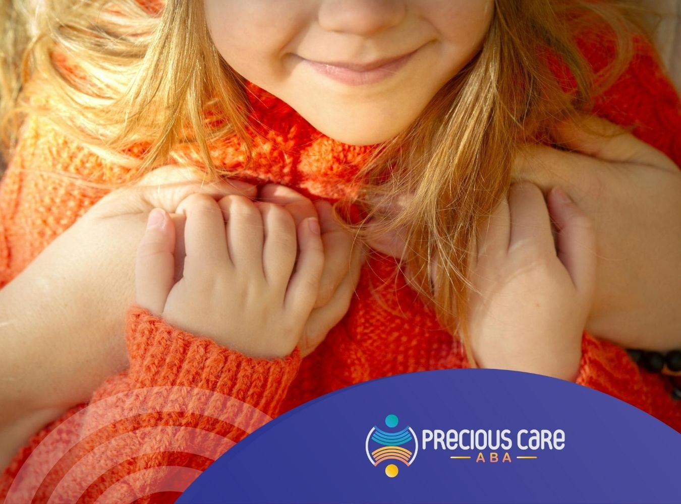 An autistic child in orange sweater holding hands close to chest with a smile during ABA therapy in Maryland.