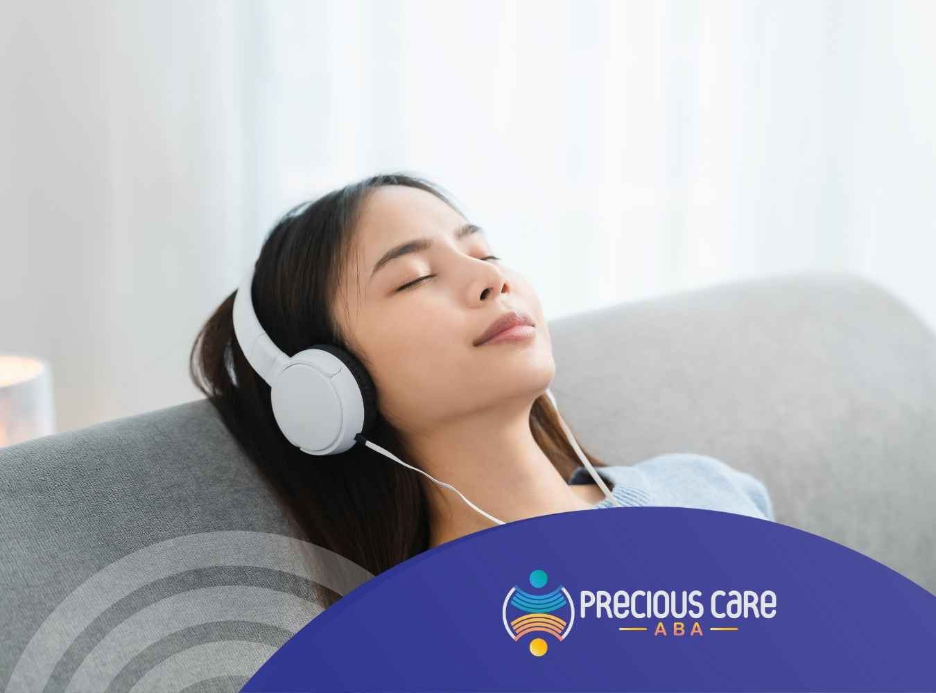 A woman with long dark hair is relaxing on a couch, eyes closed, wearing white headphones. She appears peaceful and calm, with a soft light in the background.