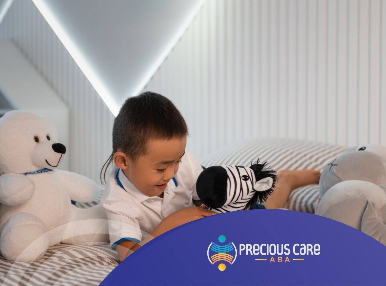 A child with autism smiling while playing with zebra stuffed animal on bed.