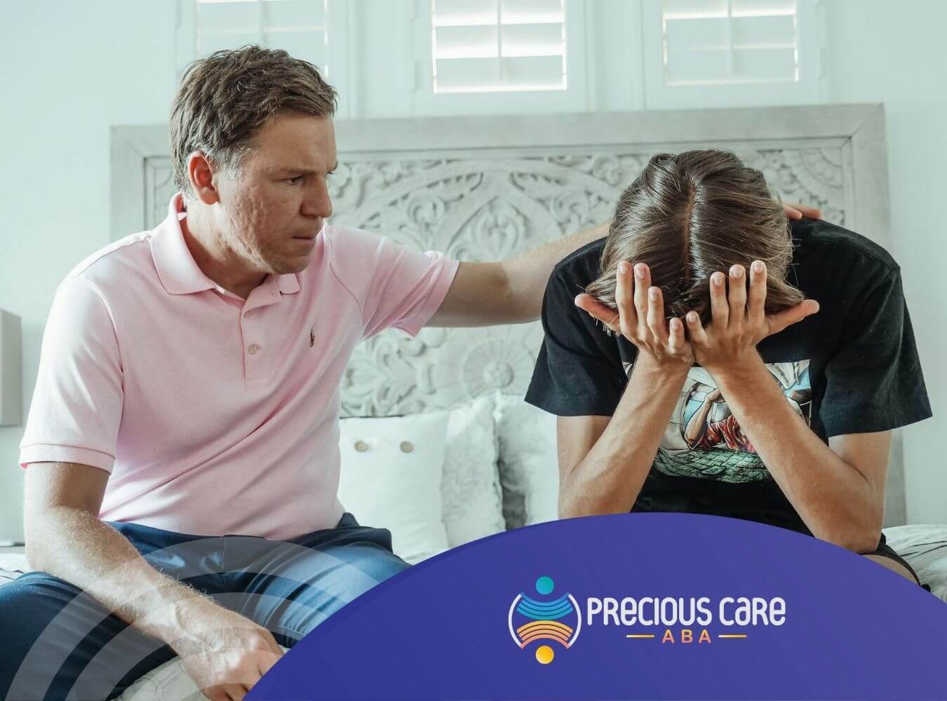 Father comforting his upset autistic teenage son sitting on bed after ABA therapy in Precious.